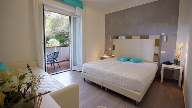 A bedroom with a bed, a nightstand, a chair, and a view of the outdoors through a sliding door. - Hotel Brigantino (Marciana)