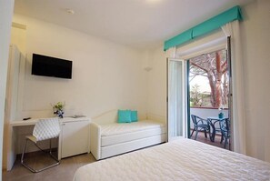 Un dormitorio con cama, escritorio y televisión. Hay un balcón con sillas y una mesa.