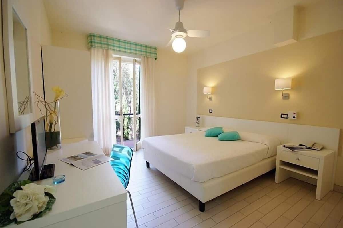 Une chambre à coucher avec un lit, des tables de chevet, un bureau avec un ordinateur et une fenêtre avec des rideaux.