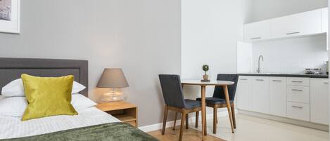 A modern hotel room with a bed, a desk, and a kitchenette.