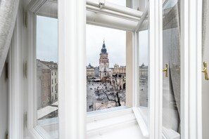 Vista attraverso una finestra su un edificio con una torre imponente, un cortile e architettura circostante.
