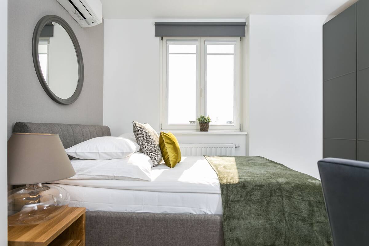 Un dormitorio con una cama, una mesita de noche con lámpara, una ventana con vistas y un radiador.