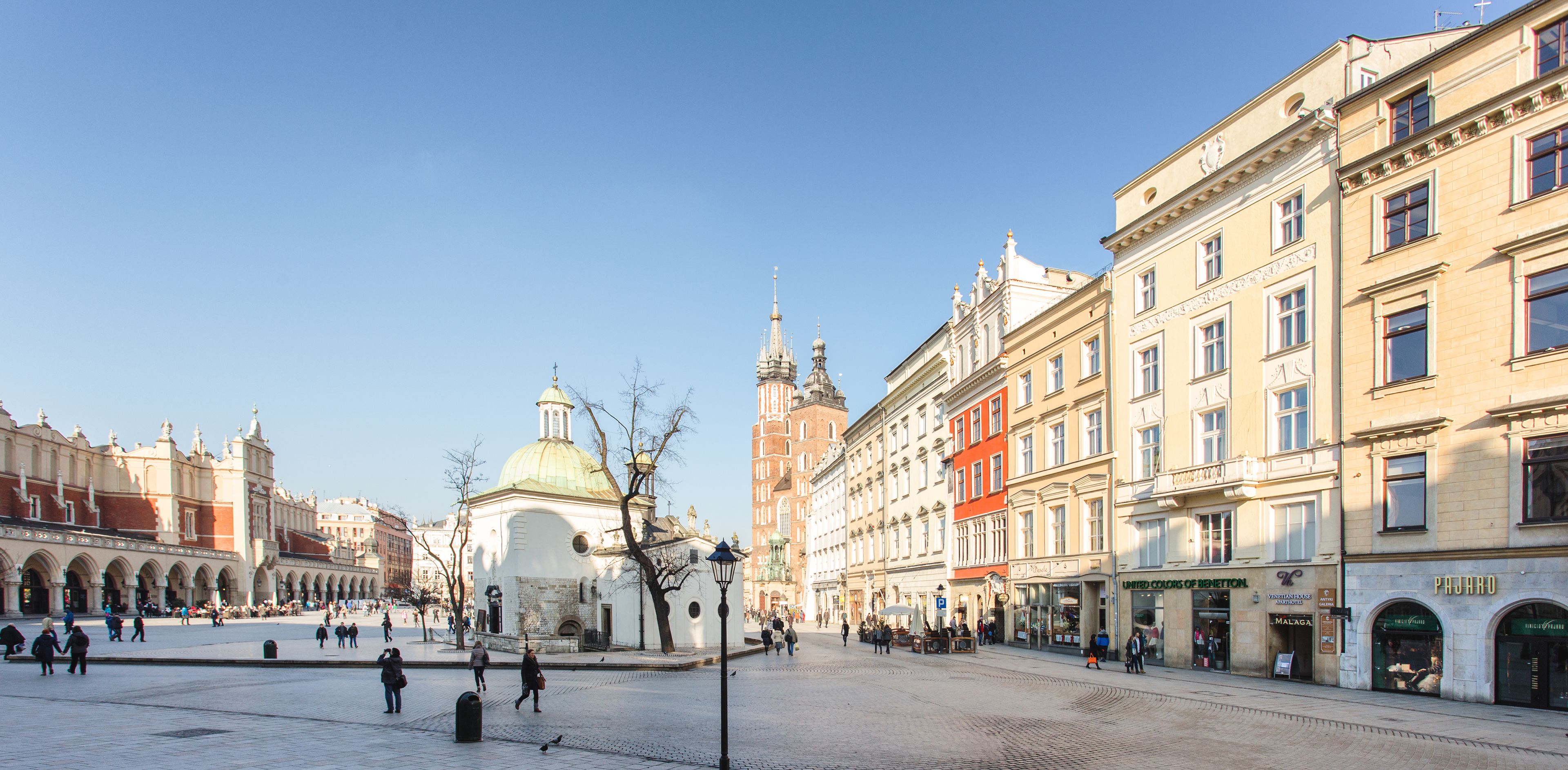 Uma praça histórica com uma igreja imponente, calçamento de pedra e arquitetura europeia tradicional.