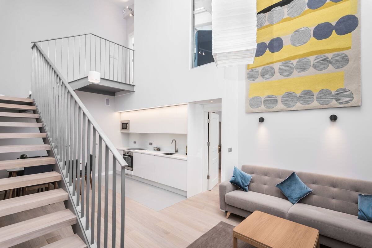 Un interior moderno con una escalera, una cocina y una sala de estar con sofá y cojines.