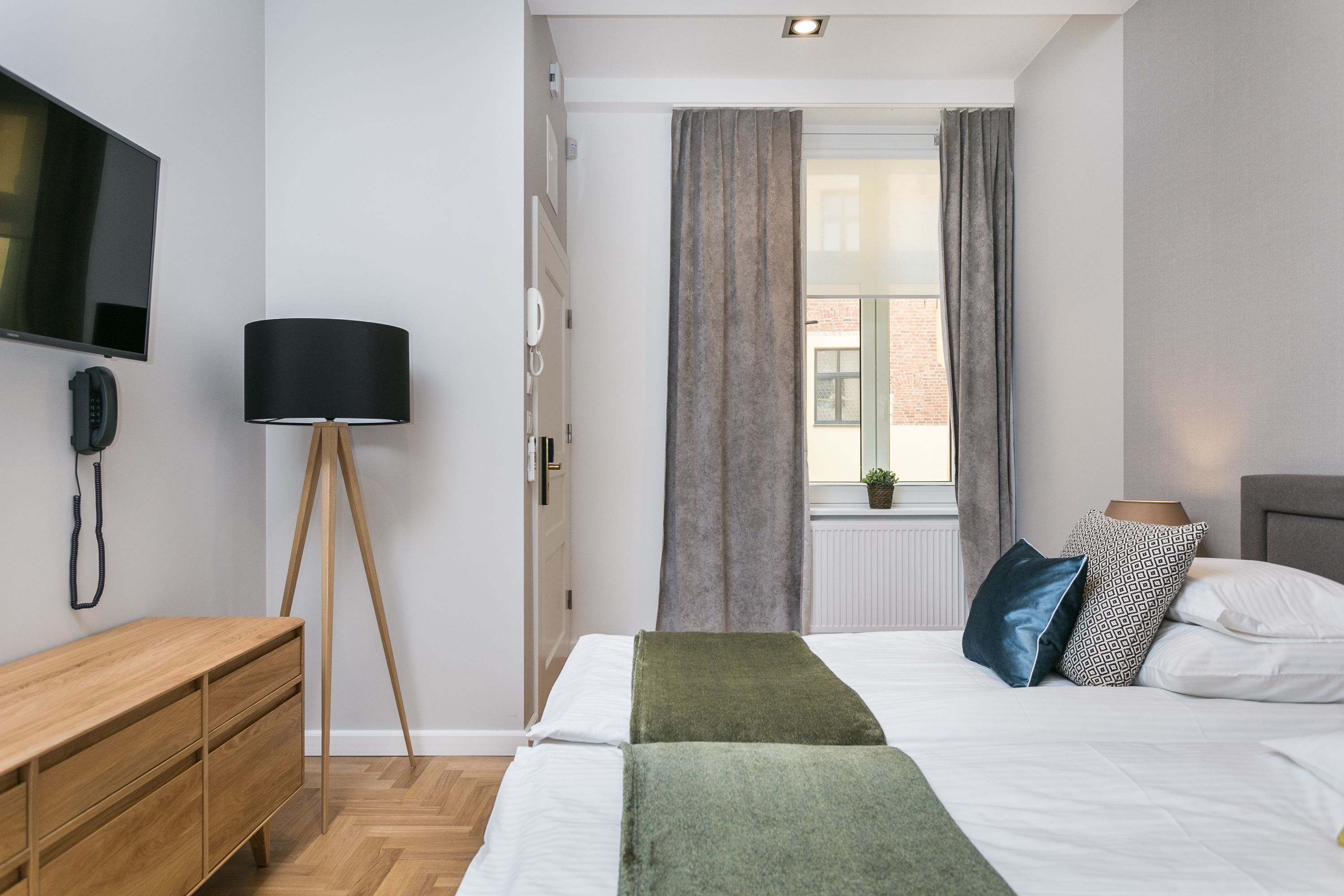A modern hotel room with a bed, bedside table, lamp, and a TV mounted on the wall.