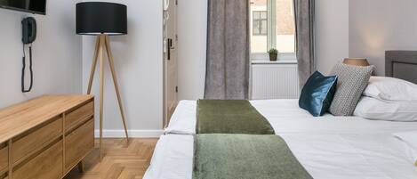 A modern hotel room with a bed, bedside table, lamp, and a TV mounted on the wall.