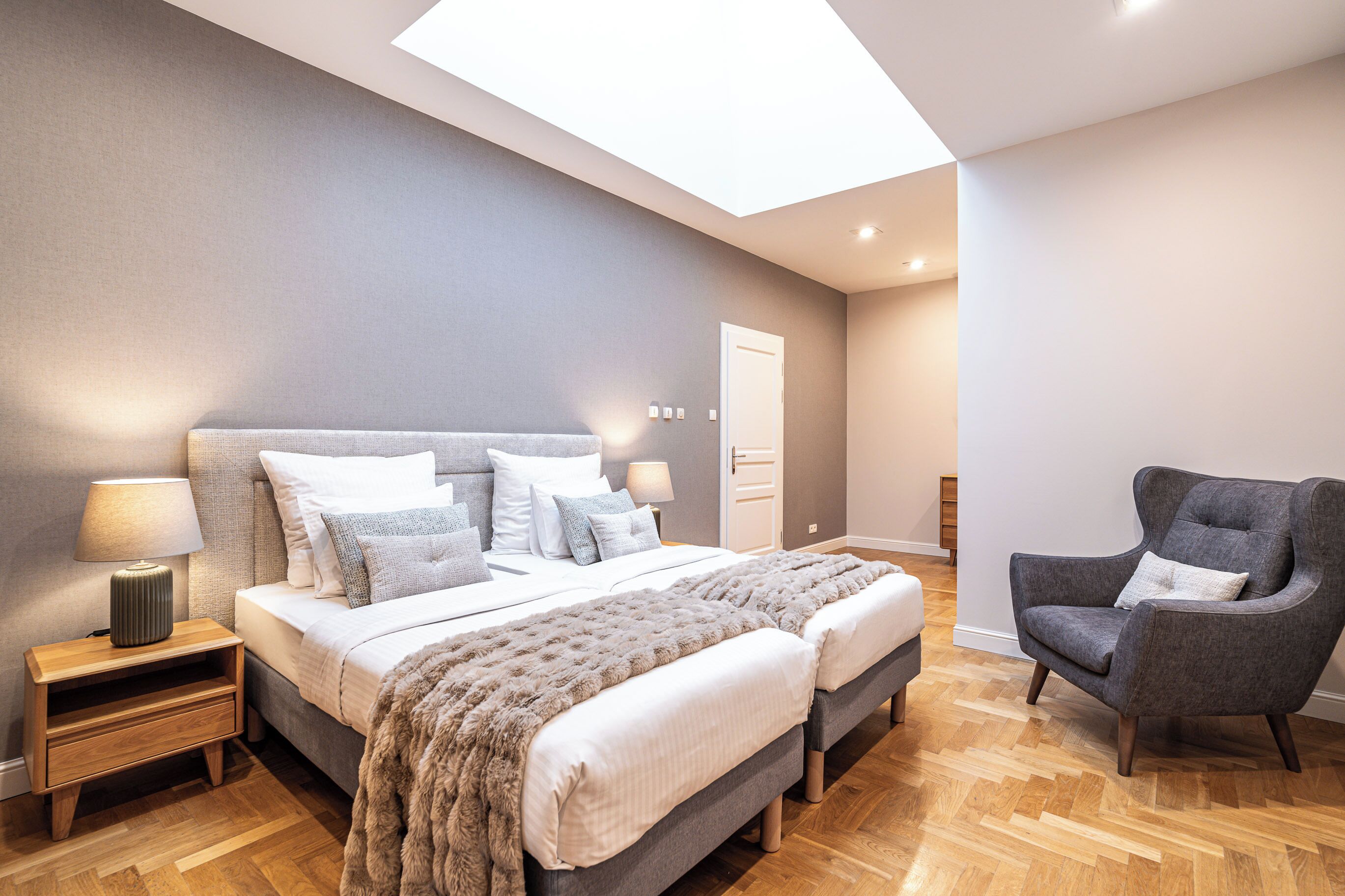 Un dormitorio moderno con una cama grande, dos mesitas de noche, una silla y un tragaluz.
