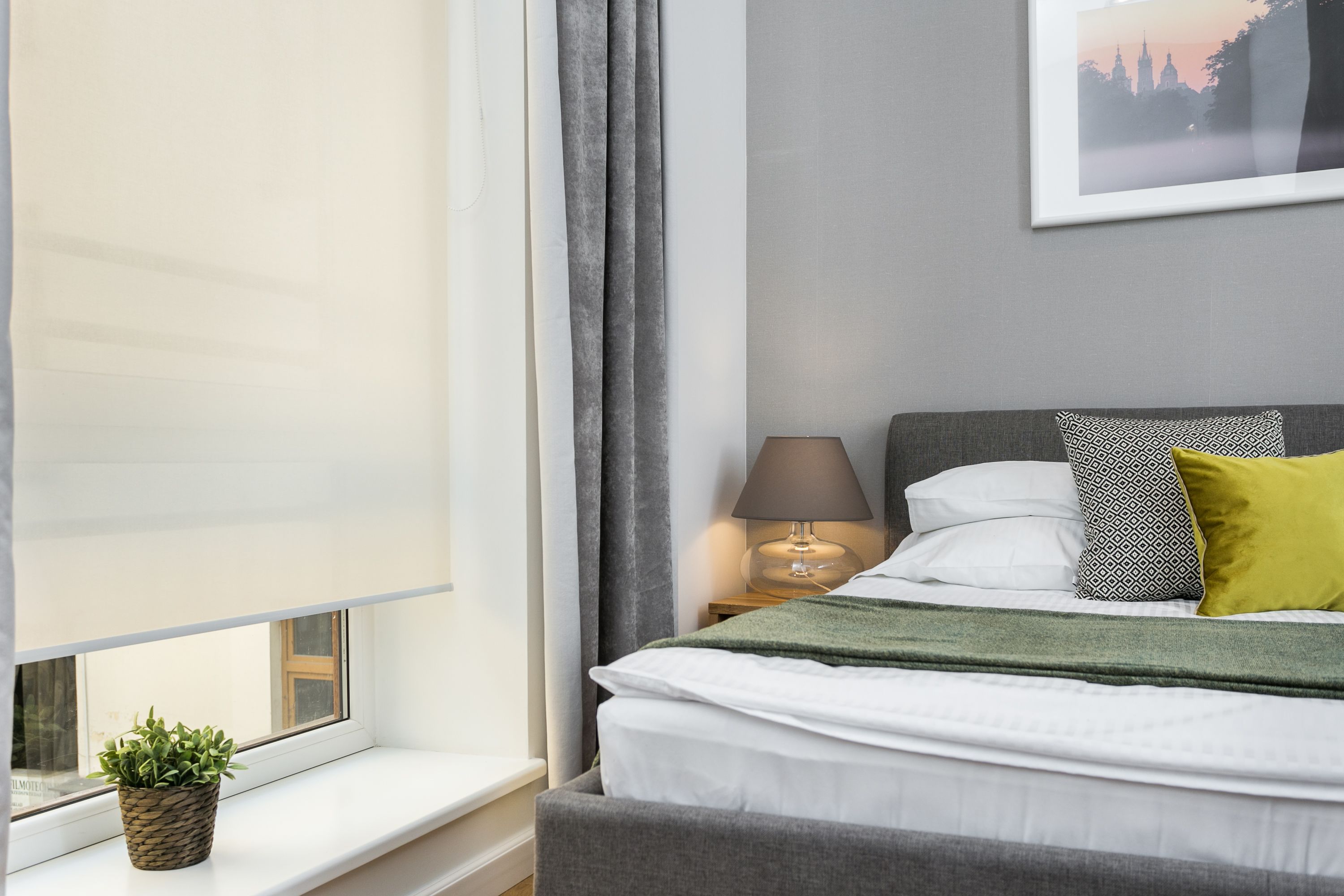 A neatly made bed with white and green bedding, a bedside lamp, and a framed picture on the wall.