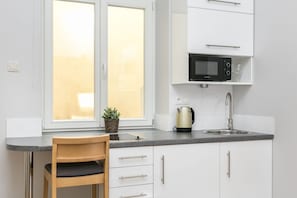 A modern kitchen with white cabinets, a black microwave, a stainless steel sink, and a wooden chair.