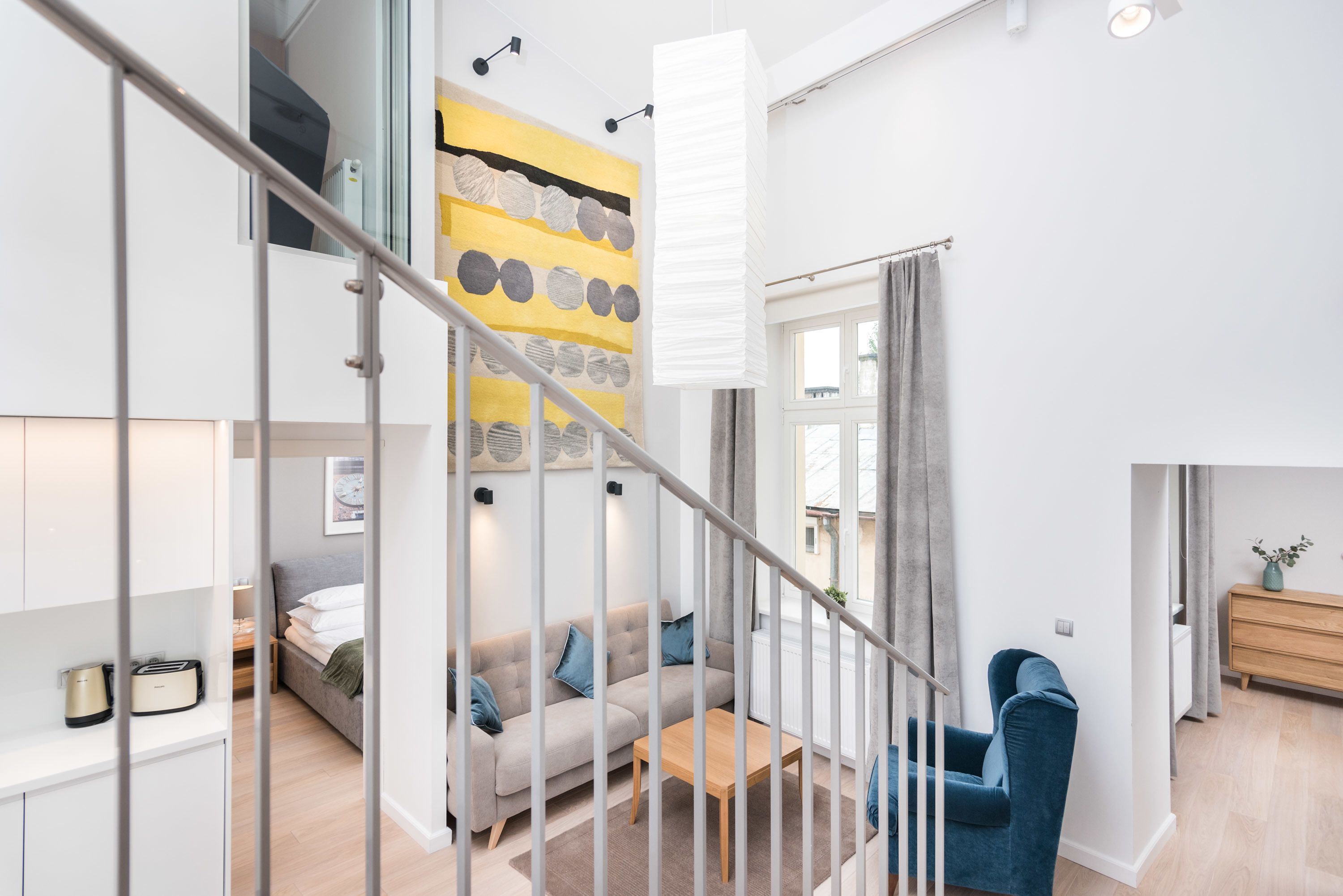 A modern living room with a sofa, a coffee table, and a blue armchair. A staircase with a railing leads to an upper level.