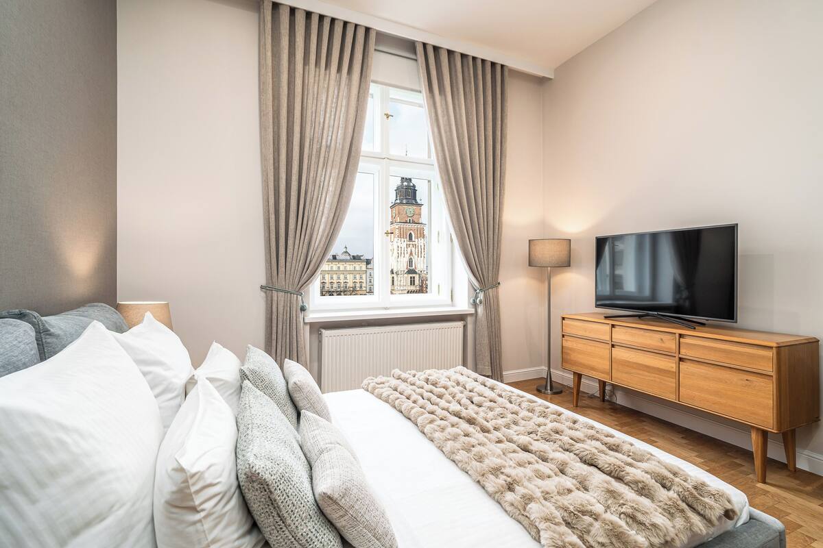 Un dormitorio con cama, televisor, cómoda y ventana con cortinas.