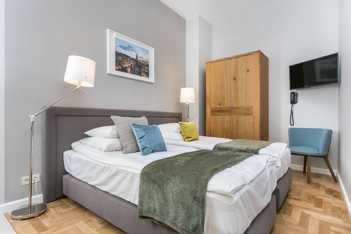Una habitación de hotel moderna con una cama, lámparas de noche, televisión y un armario.