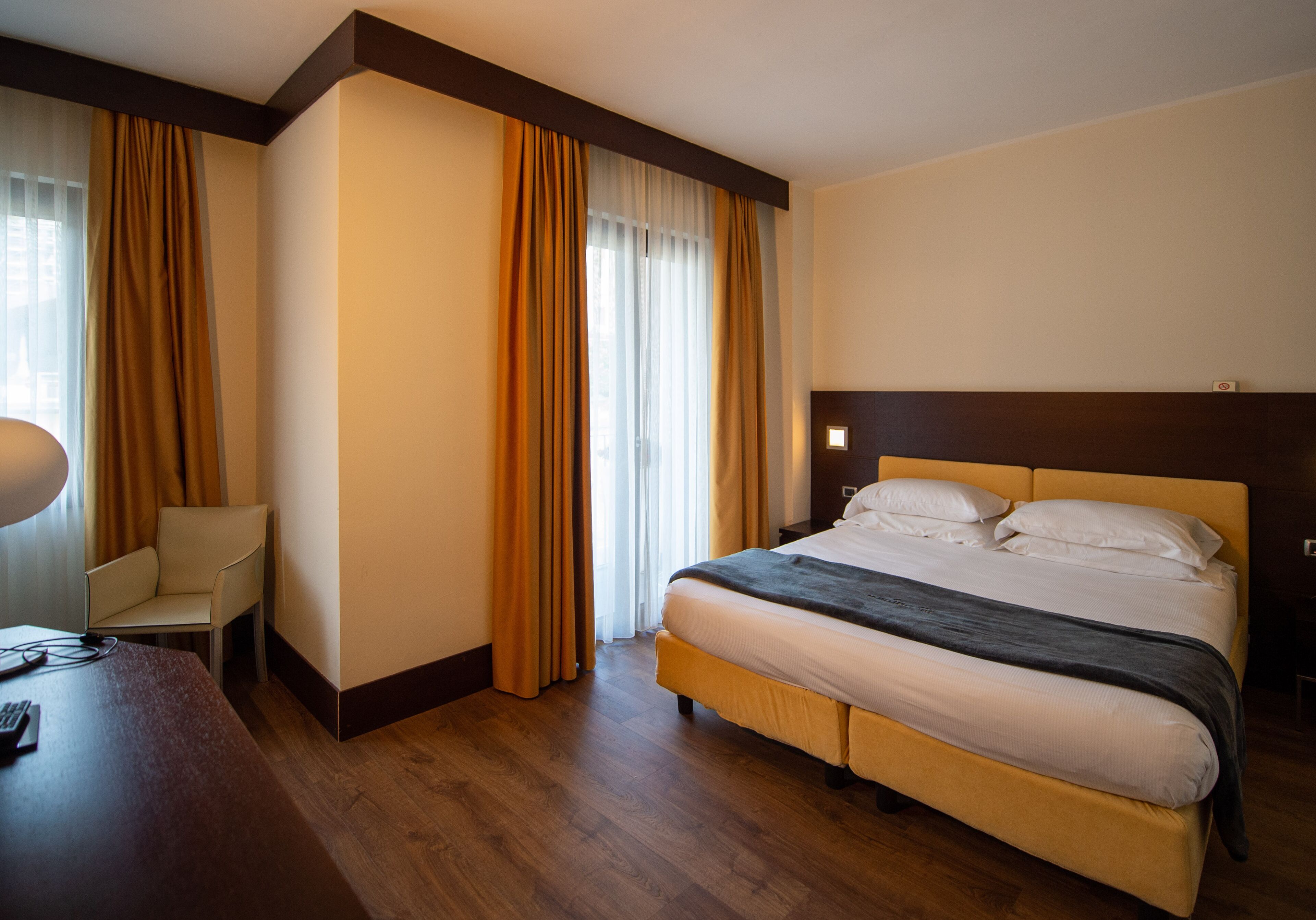 A hotel room with a bed, a chair, a desk, and a window with curtains.