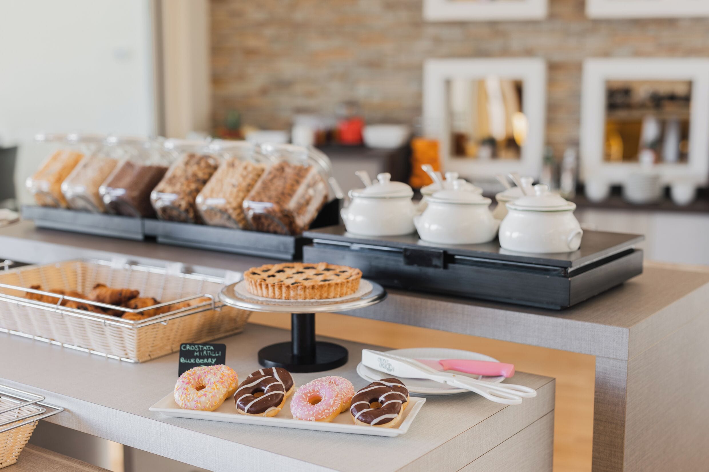Eine Bäckertheke mit Gebäcken, einer Torte und einem Schild, das Croissants, Muffins und Blaubeermuffins anzeigt.
