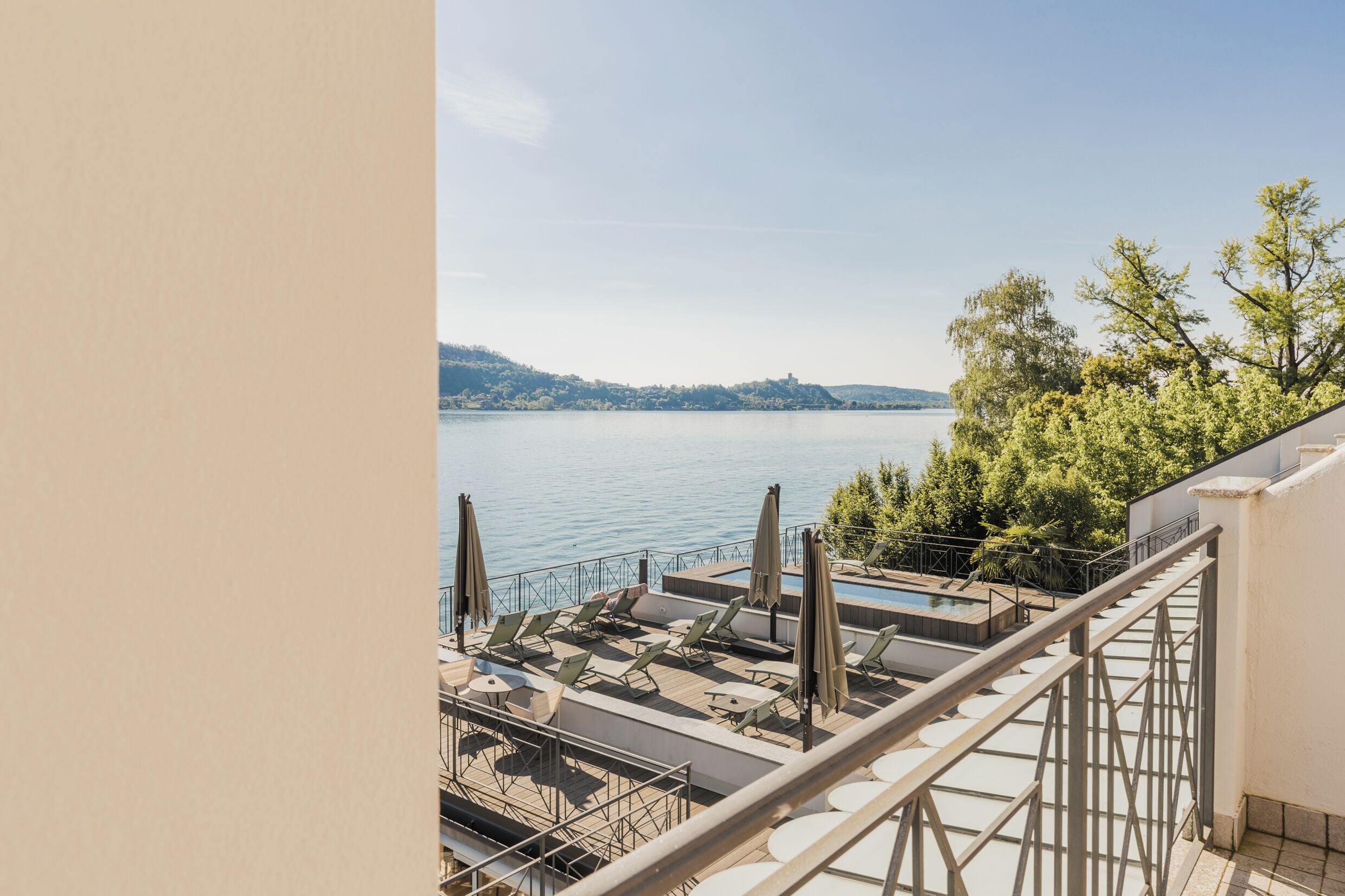 A rooftop terrace with a pool, sun loungers, and a view of a lake and hills.