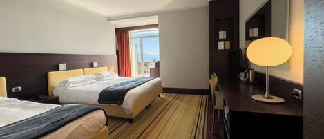 Habitación de hotel con dos camas, un ventanal grande, un escritorio con lámpara y un espejo.