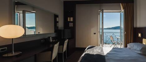 A hotel room with a bed, desk, chairs, a mirror, and a view of the sea.