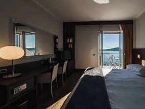 A hotel room with a bed, desk, chairs, a mirror, and a view of the sea. - Hotel Bel Sit (Meina)