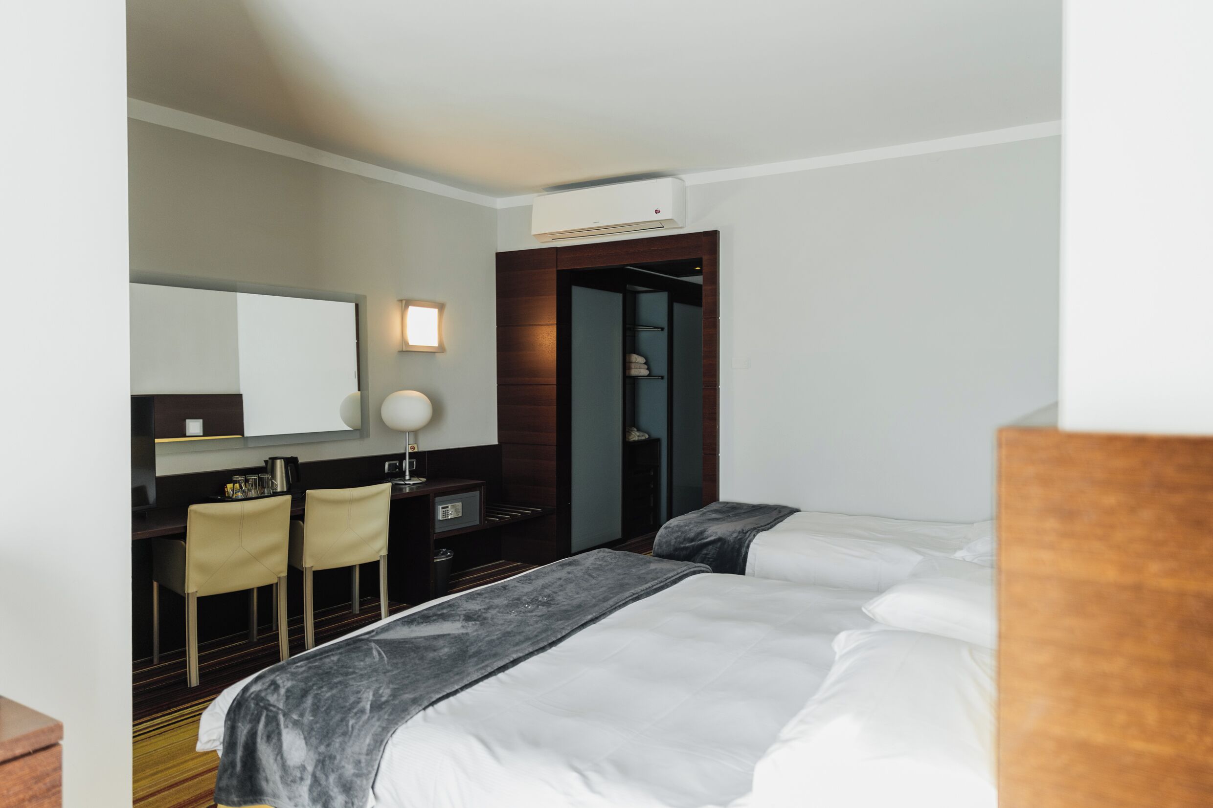 A hotel room with a bed, a desk, two chairs, a mirror, and a wardrobe.