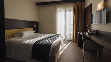 A hotel room with a bed, a desk, a chair, a TV, and a window with curtains.