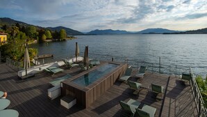 Une terrasse dotée d’une piscine rectangulaire, de chaises longues et offrant une vue sur un lac et des montagnes.