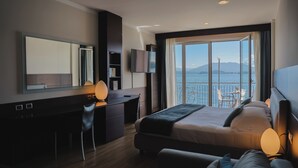 Une chambre d’hôtel moderne dotée d’un grand lit, d’un bureau, d’une chaise, d’une télévision et d’un balcon offrant une vue sur la mer.