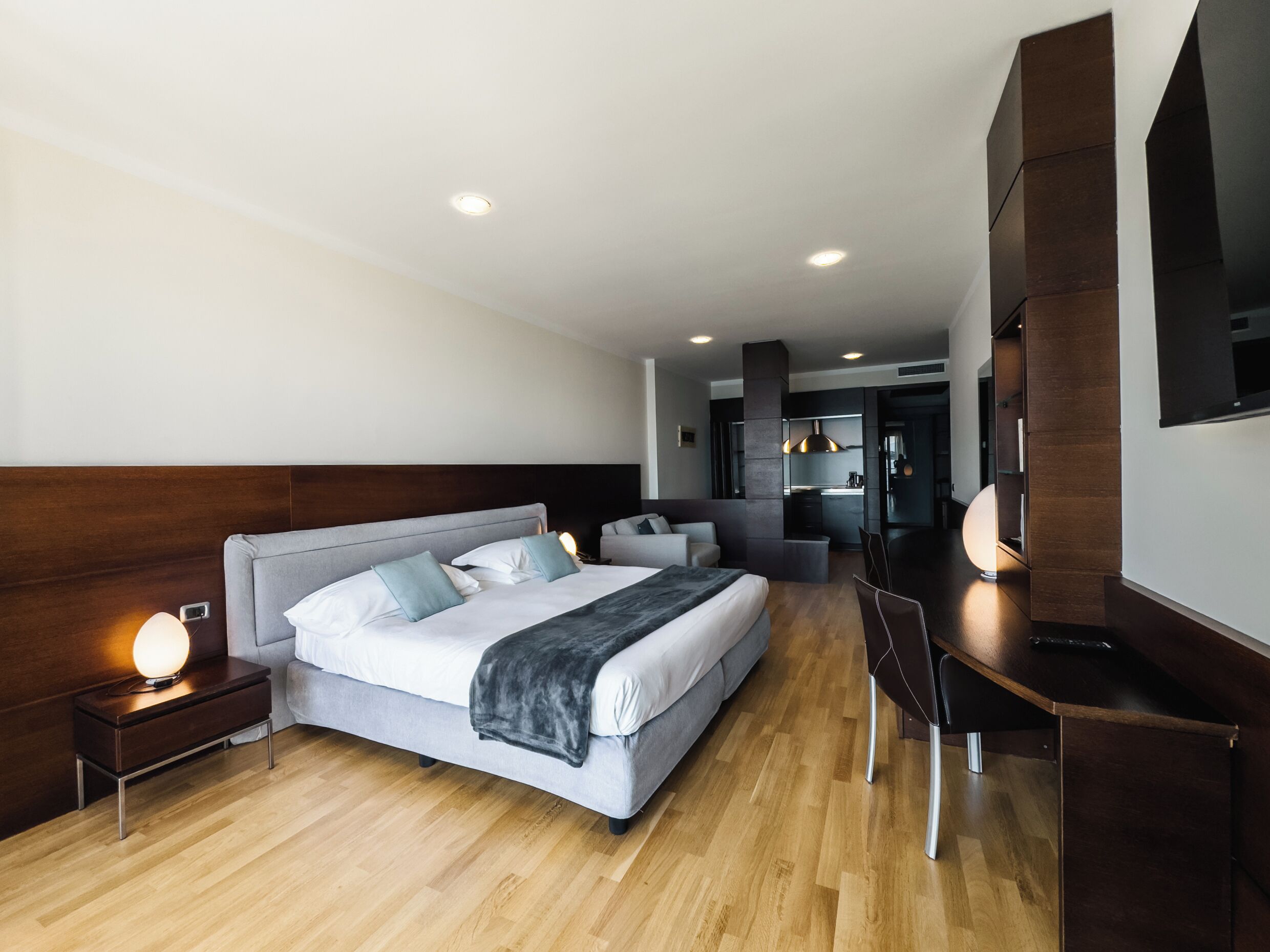 Une chambre d’hôtel moderne équipée d’un grand lit, de tables de chevet, d’un bureau et d’une kitchenette.