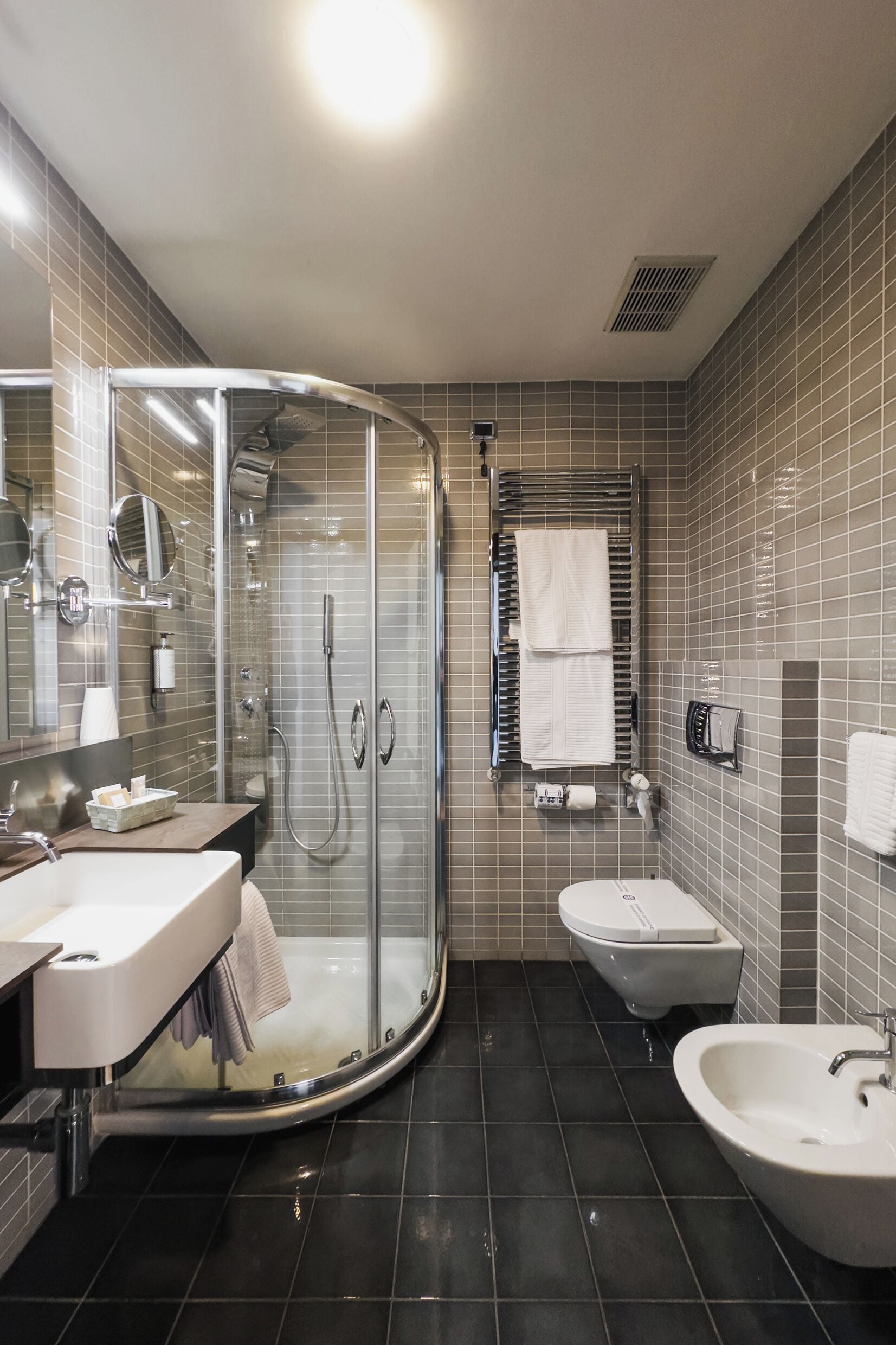 Un baño moderno con ducha envuelta en vidrio, tocador con espejo, un bidé y un lavamanos.