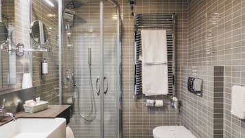 Un baño moderno con ducha envuelta en vidrio, tocador con espejo, un bidé y un lavamanos.