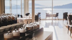 Un comptoir de petit-déjeuner avec des bocaux de granola et diverses confitures, offrant une vue panoramique sur un plan d’eau et des montagnes.