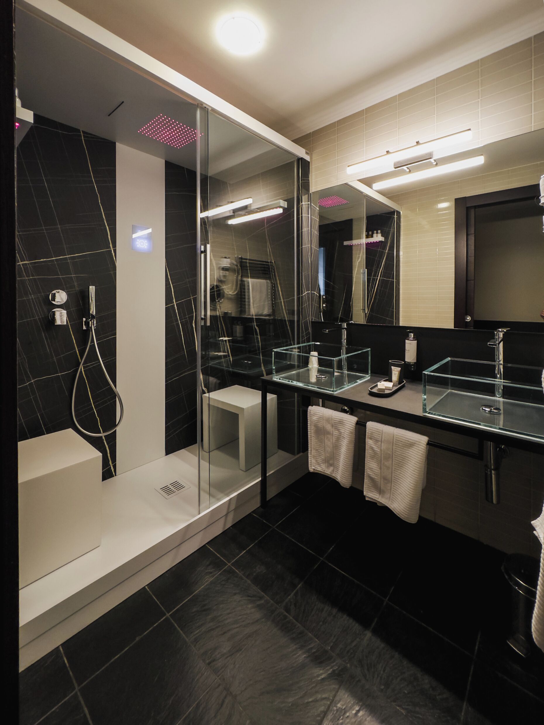 Un baño moderno con ducha envuelta en vidrio, un espejo grande y una zona de tocador separada.