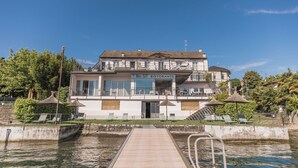 Un bâtiment situé au bord de l’eau, sur lequel on peut lire l’inscription « BEL SIT RISTORANTE », avec une terrasse dotée de chaises longues et de parasols, un ciel dégagé et un quai qui s’avance dans l’eau.