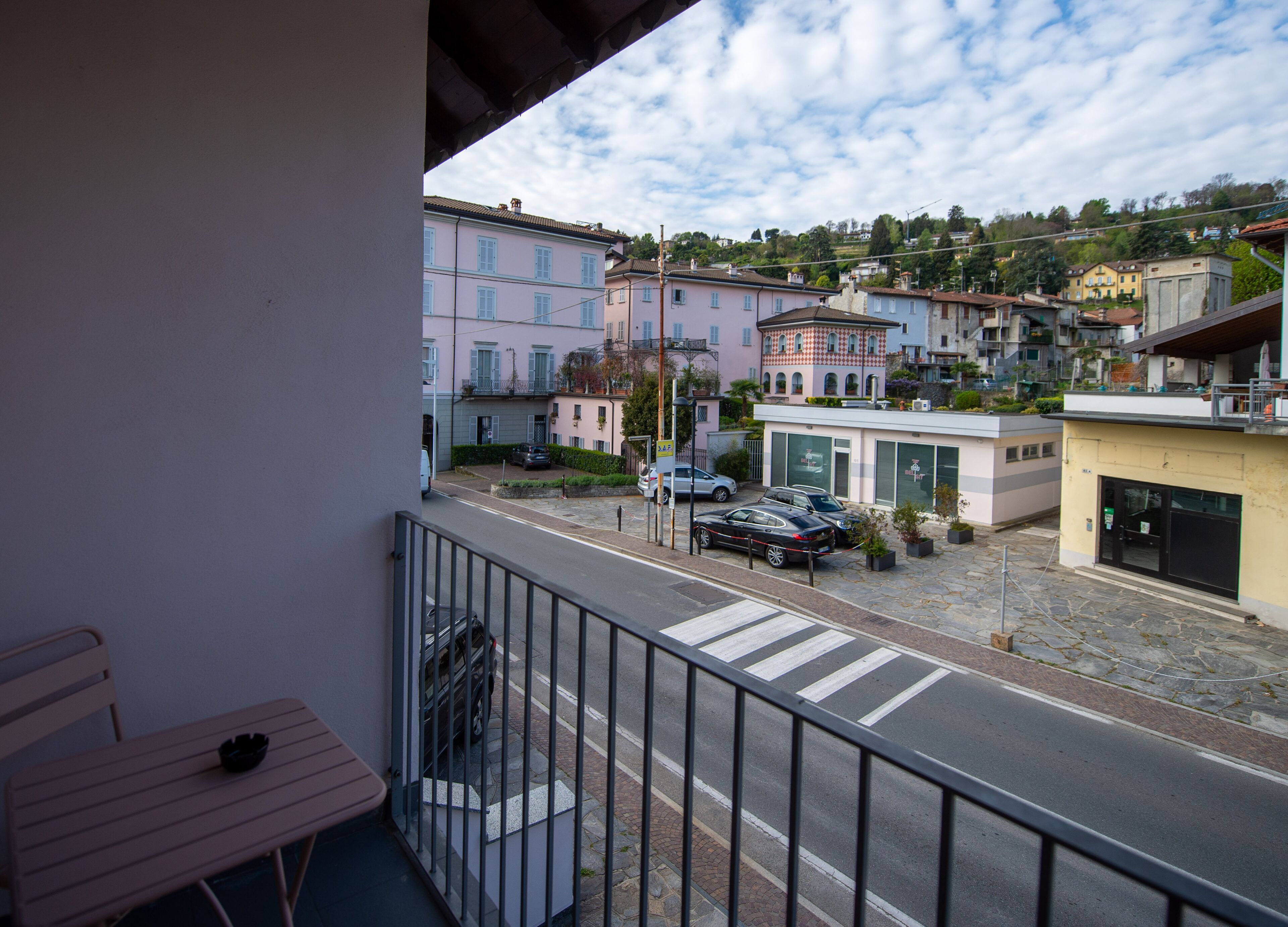A balcony with a view of a street lined with buildings, a crosswalk, and parked cars.