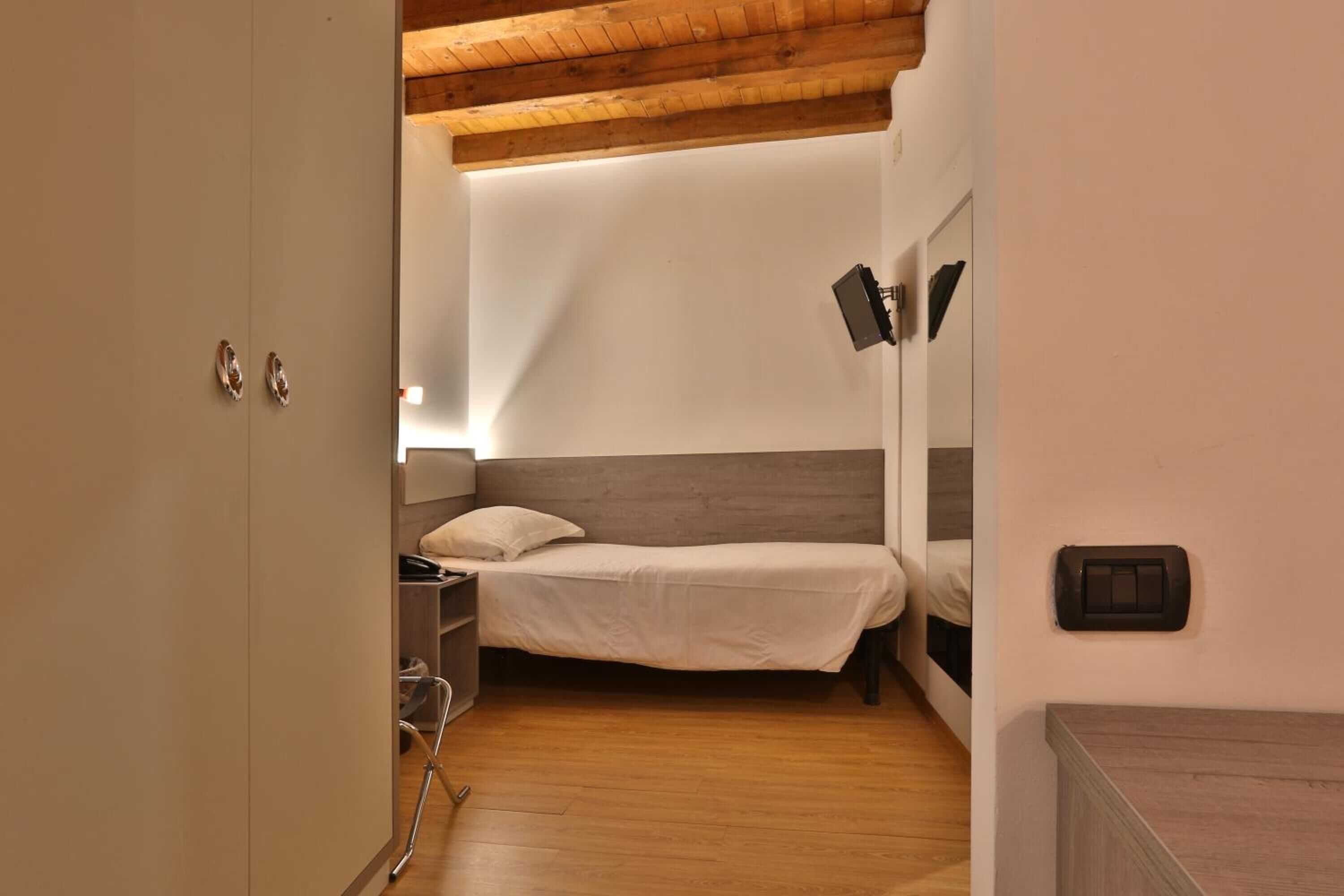 A bedroom with a bed, bedside table, lamp, and a mirror on the wall.