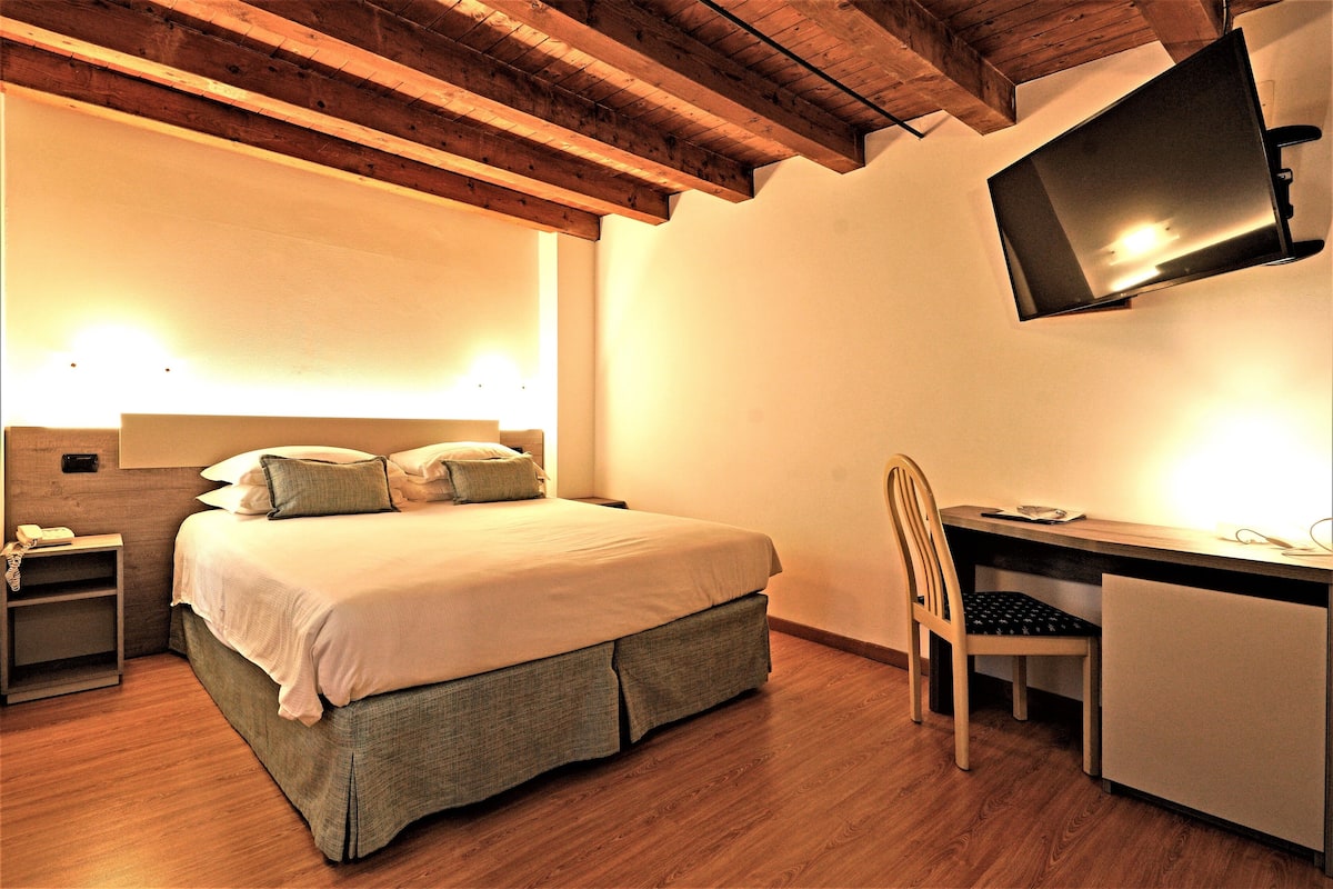 Ein Schlafzimmer mit Bett, Nachttisch, Schreibtisch, Stuhl und einem an der Wand befestigten Fernseher.