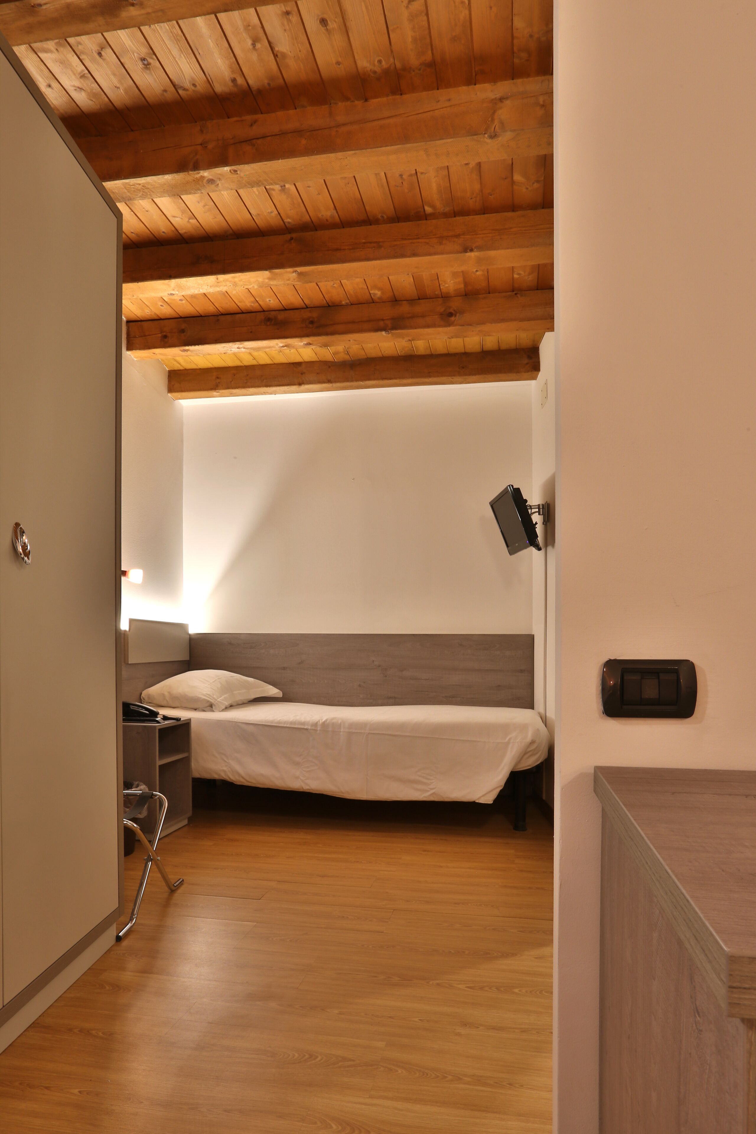 A bedroom with a wooden ceiling, a bed, a nightstand, and a wall-mounted light.