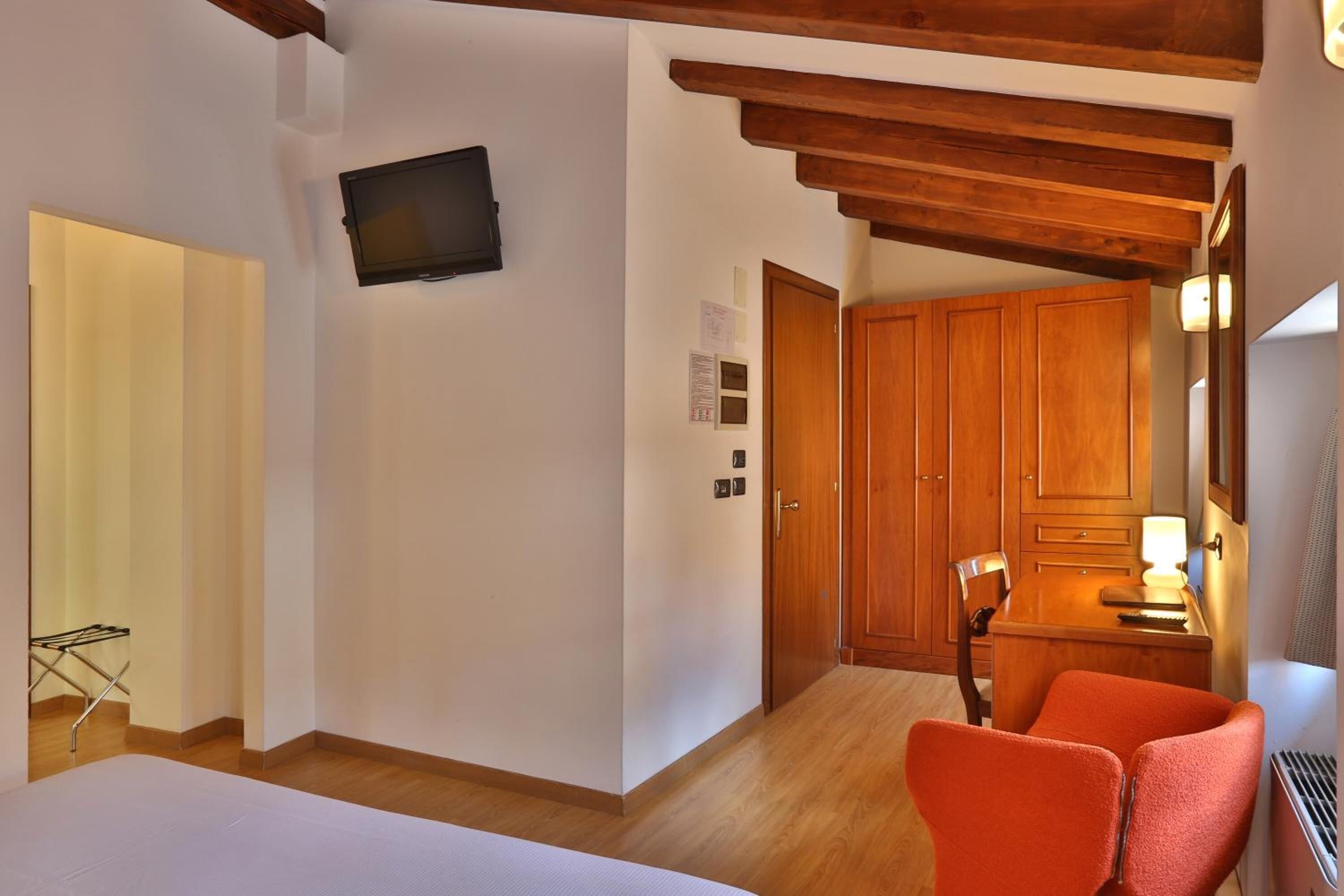 Quarto de hotel com cama, teto de madeira, TV fixada na parede e guarda-roupa de madeira.