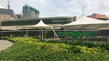 An Asian fruit market with a sign, surrounded by greenery and a large building in the background.