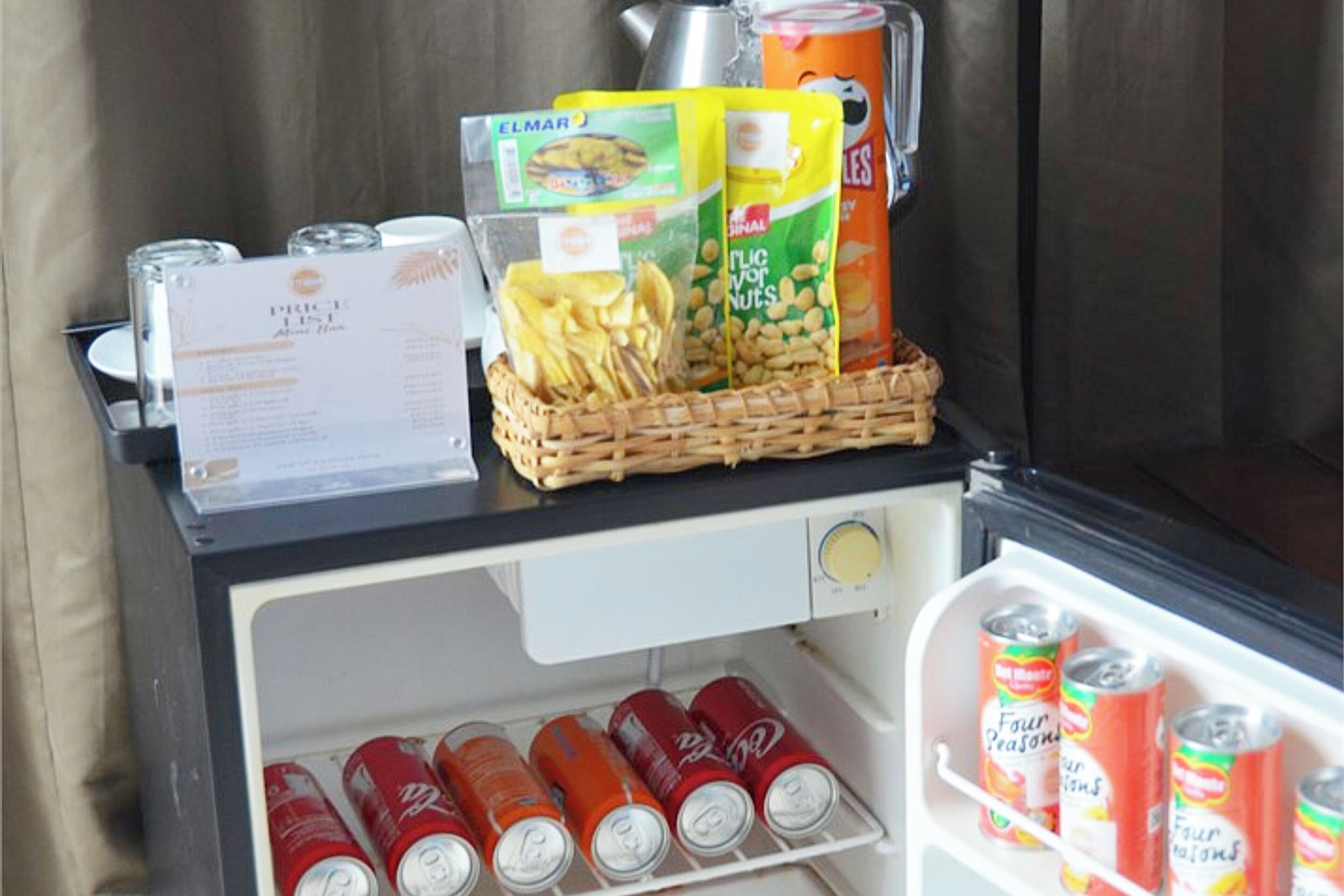 Un mini-bar contenant des en-cas, une liste de prix et plusieurs canettes de boissons gazeuses.