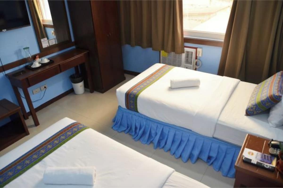 A hotel room with two beds, a desk, a TV, and a window with curtains.