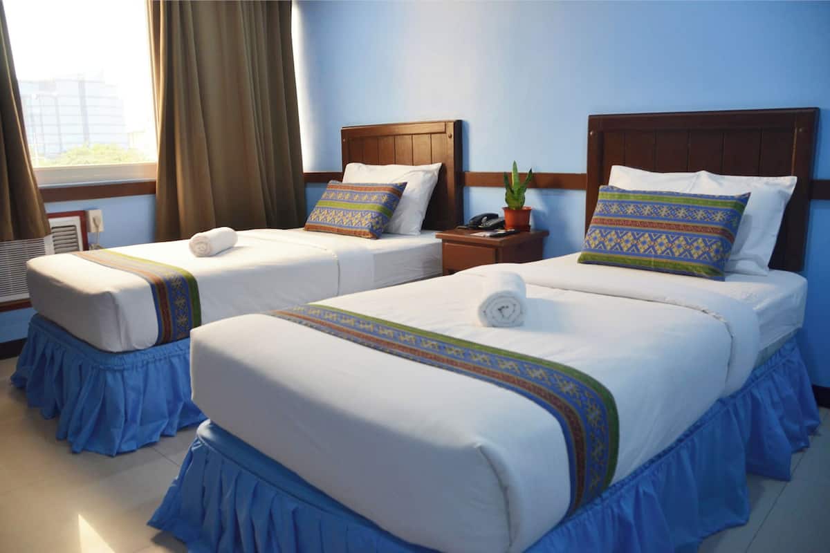 A hotel room with two beds, each with a wooden headboard, a blue skirted bed base, and patterned pillows.