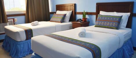A hotel room with two beds, each with a wooden headboard, a blue skirted bed base, and patterned pillows.