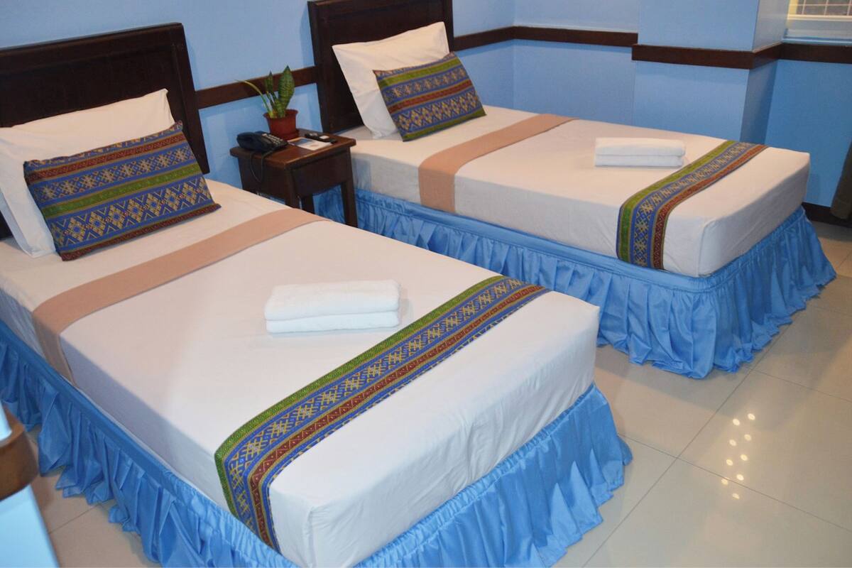 Two twin beds with blue bed skirts, white linens, and decorative pillows.