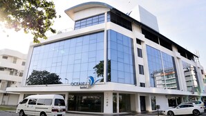 A modern hotel building with a glass facade, a white van parked in front, and a car parked to the side. - Oceania Hotel (Kota Kinabalu)