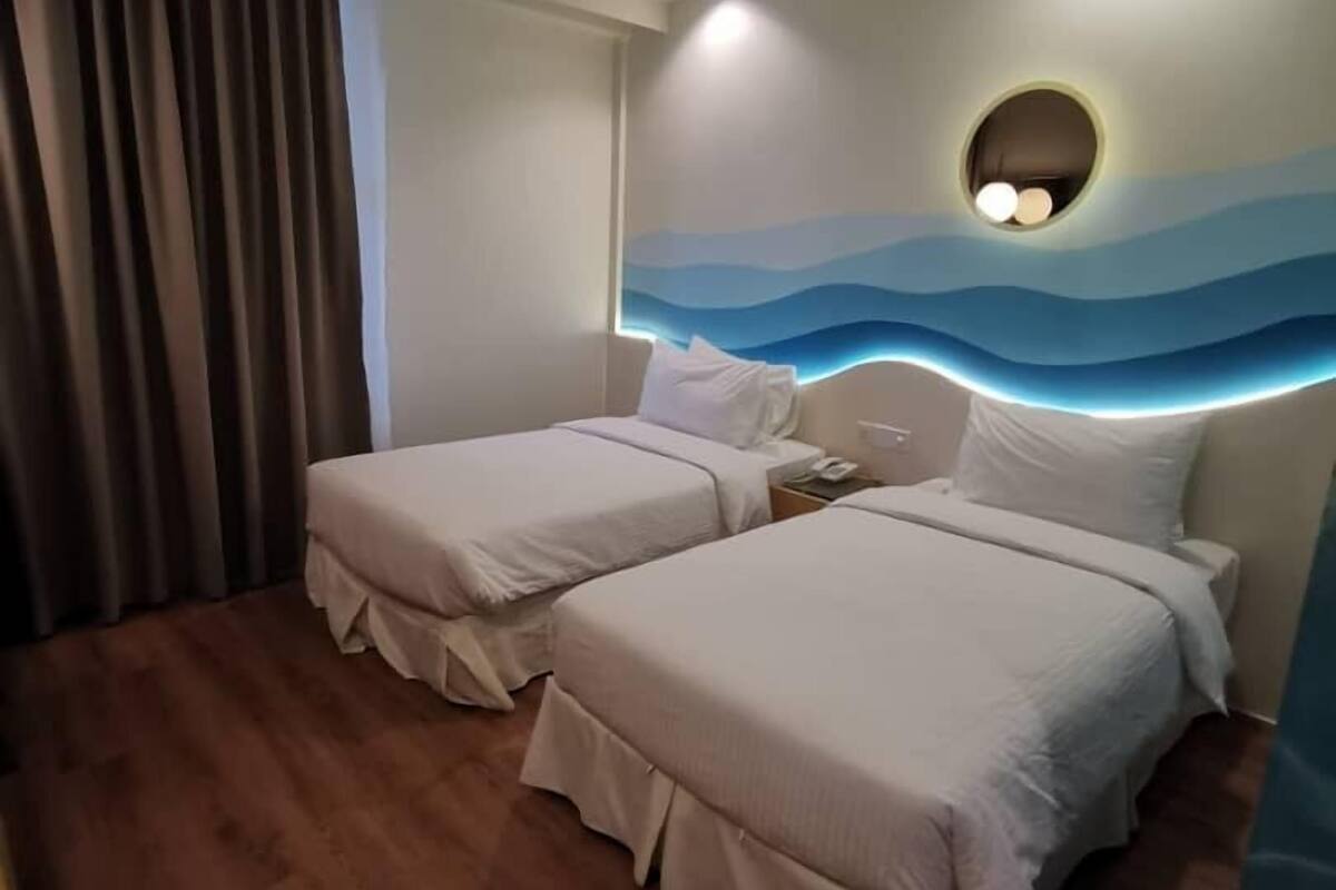 A hotel room with two beds, a wooden floor, a large window with curtains, and a wall mural.