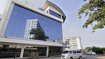 A modern building with a glass facade, a flat roof, and a parking area with a white van.