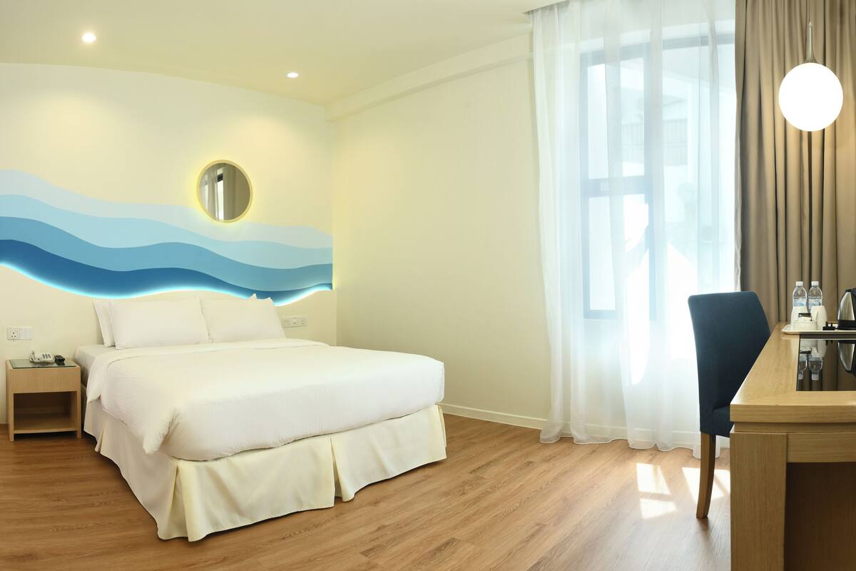 A hotel room with a bed, bedside table, and a desk with a chair.