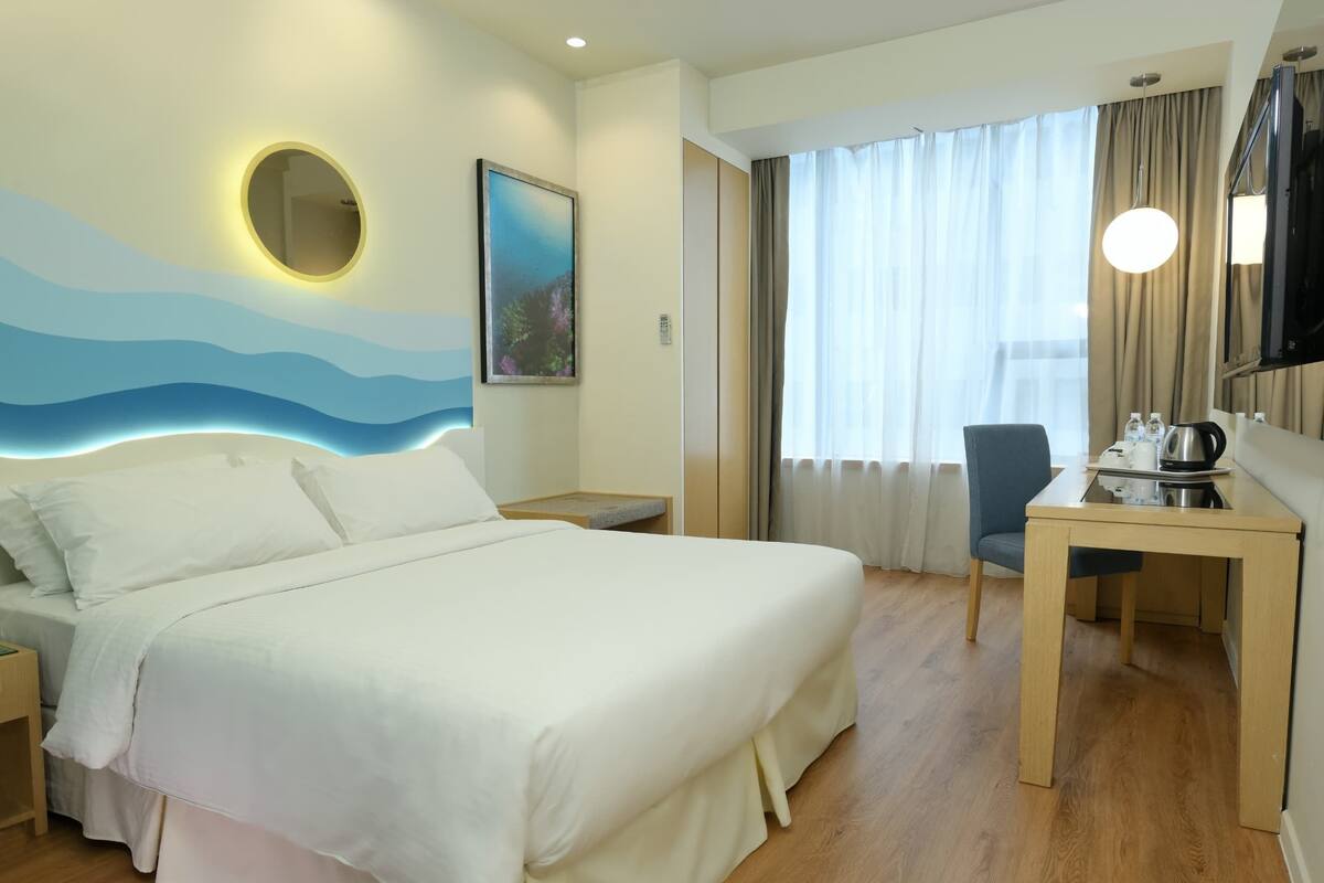A hotel room with a large bed, a desk with a chair, a TV, and a painting on the wall.