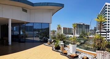 Un hotel moderno con terraza en la azotea que cuenta con una cubierta de madera, plantas en macetas y una entrada de cristal.