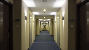 A hotel hallway with doors on both sides, numbered signs, and a carpeted floor. - Oceania Hotel (Kota Kinabalu)